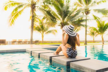 Güzel bir Asyalı kadın portresi, gün batımında palmiye ağacıyla birlikte havuz kenarında dinleniyor ya da tatil için gün doğumunda dinleniyor.