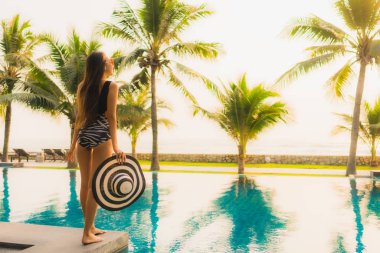 Güzel bir Asyalı kadın portresi, gün batımında palmiye ağacıyla birlikte havuz kenarında dinleniyor ya da tatil için gün doğumunda dinleniyor.