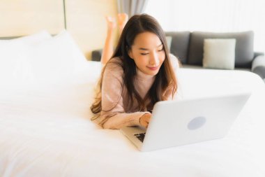 Yatak odasının iç kısmında dizüstü bilgisayar kullanan güzel Asyalı kadın portresi.