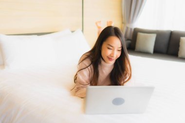 Yatak odasının iç kısmında dizüstü bilgisayar kullanan güzel Asyalı kadın portresi.