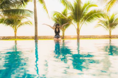 Güzel bir Asyalı kadın portresi, gün batımında palmiye ağacıyla birlikte havuz kenarında dinleniyor ya da tatil için gün doğumunda dinleniyor.
