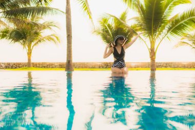 Güzel bir Asyalı kadın portresi, gün batımında palmiye ağacıyla birlikte havuz kenarında dinleniyor ya da tatil için gün doğumunda dinleniyor.