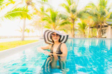 Güzel bir Asyalı kadın portresi, gün batımında palmiye ağacıyla birlikte havuz kenarında dinleniyor ya da tatil için gün doğumunda dinleniyor.