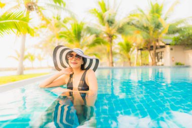 Güzel bir Asyalı kadın portresi, gün batımında palmiye ağacıyla birlikte havuz kenarında dinleniyor ya da tatil için gün doğumunda dinleniyor.