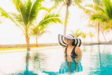 Güzel bir Asyalı kadın portresi, gün batımında palmiye ağacıyla birlikte havuz kenarında dinleniyor ya da tatil için gün doğumunda dinleniyor.