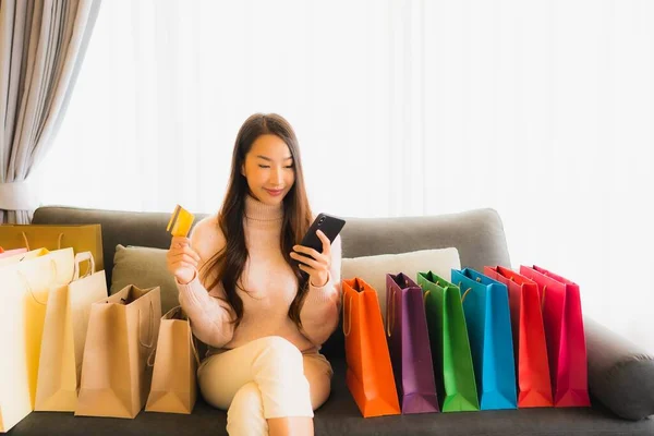 아름다운 아시아 거실에 쇼핑백 주위에서 온라인 쇼핑을 노트북이나 스마트폰을 사용하는 — 스톡 사진