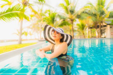 Güzel bir Asyalı kadın portresi, gün batımında palmiye ağacıyla birlikte havuz kenarında dinleniyor ya da tatil için gün doğumunda dinleniyor.