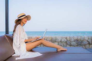 Plaj denizi çevresinde çalışmak için dizüstü bilgisayarı kullanan Asyalı genç bir kadının portresi.