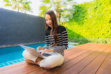 Genç Asyalı bir kadının portresi oteldeki yüzme havuzunda dizüstü bilgisayar kullanıyor.