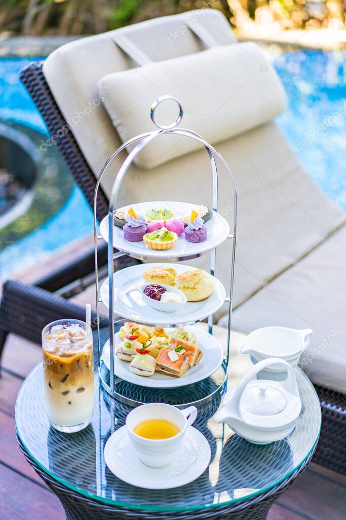 Afternoon tea set with latte coffee and hot tea on table neary chair around swimming pool in hotel resort