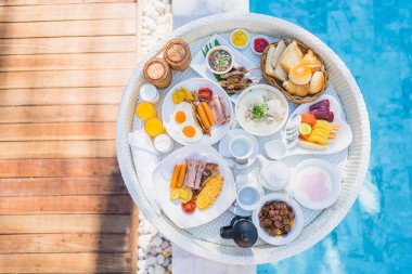 Kızarmış yumurta omletli, jambonlu, meyveli, sütlü kahveli ve yüzme havuzlu bir tepside yüzen kahvaltı.