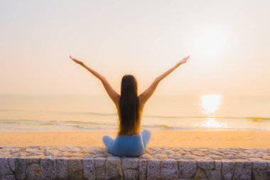 Genç Asyalı kadının portresi sağlık için gün doğumunda deniz kıyısı okyanusunda meditasyon yapıyor.