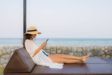 Açık deniz okyanusunda akıllı cep telefonu kullanan Asyalı genç bir kadının portresi.