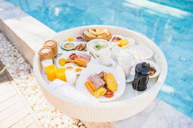 Kızarmış yumurta omletli, jambonlu, meyveli, sütlü kahveli ve yüzme havuzlu bir tepside yüzen kahvaltı.