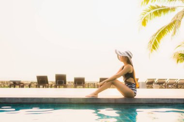 Güzel bir Asyalı kadın portresi, gün batımında palmiye ağacıyla birlikte havuz kenarında dinleniyor ya da tatil için gün doğumunda dinleniyor.