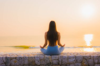 Genç Asyalı kadının portresi sağlık için gün doğumunda deniz kıyısı okyanusunda meditasyon yapıyor.