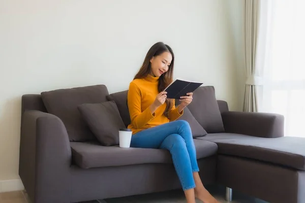 Portrait young asian woman read book on sofa chair with pillow in living room interior