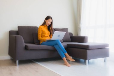 Genç Asyalı bir kadının oturma odasında çalışmak için dizüstü bilgisayar defteri kullanmasının portresi.