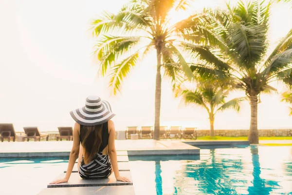 美しい若いアジアの女性は 夕日やレジャー休暇のための日の出でヤシの木とホテルのリゾートで屋外スイミングプールの周りにリラックス — ストック写真