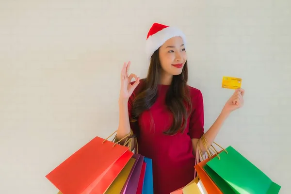 肖像画の美しい若いアジアの女性は ショッピングバッグスマート携帯電話とクレジットカードでクリスマスサンタの帽子を着用 — ストック写真