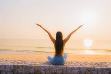 Genç Asyalı kadının portresi sağlık için gün doğumunda deniz kıyısı okyanusunda meditasyon yapıyor.