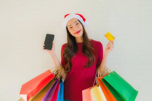 肖像画の美しい若いアジアの女性は ショッピングバッグスマート携帯電話とクレジットカードでクリスマスサンタの帽子を着用 — ストック写真
