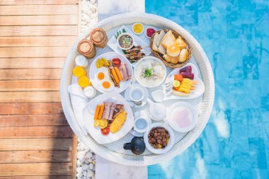 Kızarmış yumurta omletli, jambonlu, meyveli, sütlü kahveli ve yüzme havuzlu bir tepside yüzen kahvaltı.