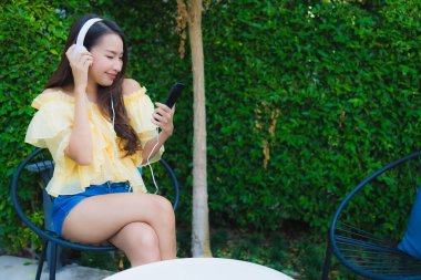 Genç Asyalı kadın kulaklıklı akıllı cep telefonunu açık hava bahçe manzaralı müzik için kullanıyor.