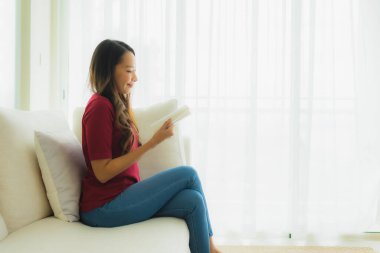 Güzel bir Asyalı kadın portresi oturma odasındaki koltukta kitap okuyor.