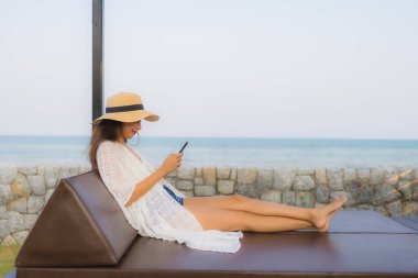 Açık deniz okyanusunda akıllı cep telefonu kullanan Asyalı genç bir kadının portresi.