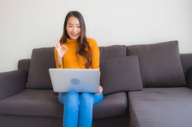 Genç Asyalı bir kadının oturma odasında çalışmak için dizüstü bilgisayar defteri kullanmasının portresi.