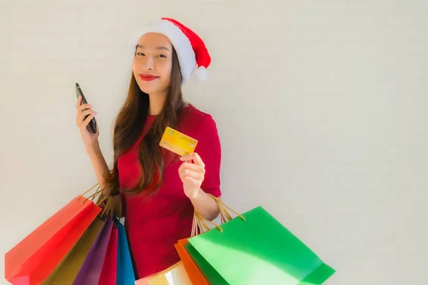 肖像画の美しい若いアジアの女性は ショッピングバッグスマート携帯電話とクレジットカードでクリスマスサンタの帽子を着用 — ストック写真