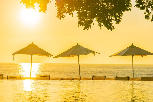 日没や旅行休暇のための日の出時に屋外スイミングプールの周りに傘と椅子と美しい熱帯屋外ビーチの海の海 — ストック写真