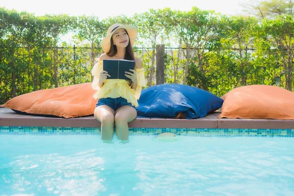 Portrait young asian woman read book around outdoor swimming pool in hotel resort