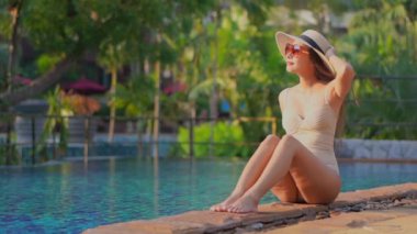 Güzel Asyalı bir kadının, tatil için otel tatil beldesinde yüzme havuzunda dinlendiği görüntüler.