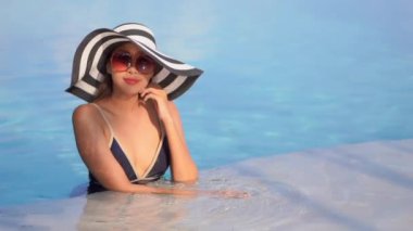 Güzel Asyalı bir kadının, tatil için otel tatil beldesinde yüzme havuzunda dinlendiği görüntüler.