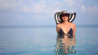 Güzel Asyalı bir kadının, tatil için otel tatil beldesinde yüzme havuzunda dinlendiği görüntüler.