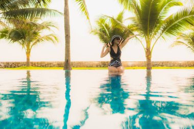 Güzel bir Asyalı kadın portresi, gün batımında palmiye ağacıyla birlikte havuz kenarında dinleniyor ya da tatil için gün doğumunda dinleniyor.