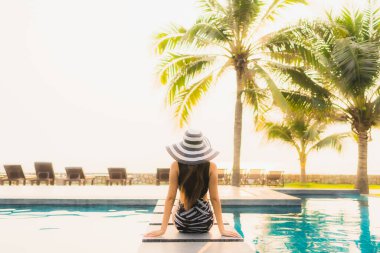 Güzel bir Asyalı kadın portresi, gün batımında palmiye ağacıyla birlikte havuz kenarında dinleniyor ya da tatil için gün doğumunda dinleniyor.