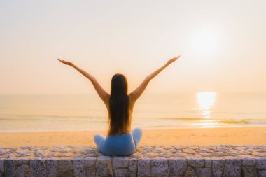 Genç Asyalı kadının portresi sağlık için gün doğumunda deniz kıyısı okyanusunda meditasyon yapıyor.