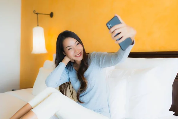 Portrait beautiful young asian woman using mobile cell phone on bed with coffee cup in bedroom interior