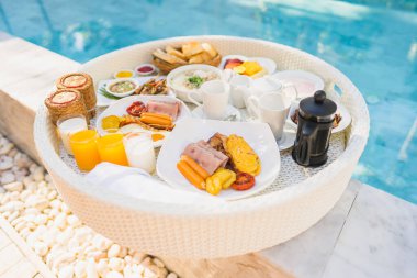 Kızarmış yumurta omletli, jambonlu, meyveli, sütlü kahveli ve yüzme havuzlu bir tepside yüzen kahvaltı.