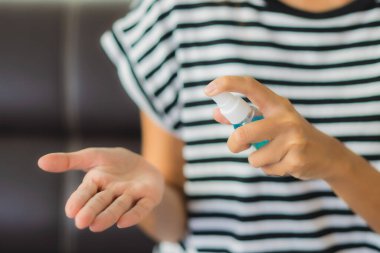Güzel Asyalı genç bir kadının portresi Coronavirus 'tan elini temizlemek için alkol spreyi kullanıyor ya da evde covid19 kullanıyor.