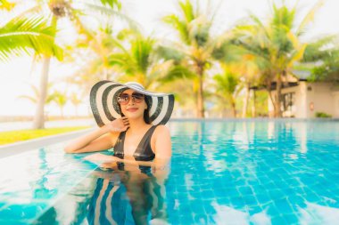 Güzel bir Asyalı kadın portresi, gün batımında palmiye ağacıyla birlikte havuz kenarında dinleniyor ya da tatil için gün doğumunda dinleniyor.