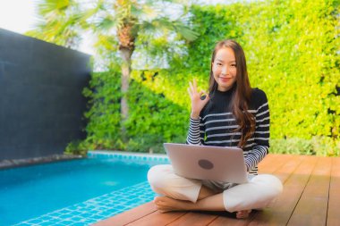 Genç Asyalı bir kadının portresi oteldeki yüzme havuzunda dizüstü bilgisayar kullanıyor.