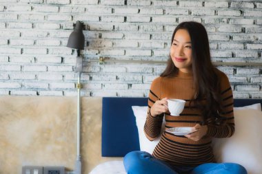 Yatak odasının iç tarafında, kahve fincanı olan Asyalı genç bir kadın.