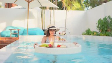 Güzel Asyalı bir kadının, tatil için otel tatil beldesinde yüzme havuzunda dinlendiği görüntüler.