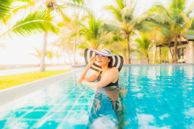 Güzel bir Asyalı kadın portresi, gün batımında palmiye ağacıyla birlikte havuz kenarında dinleniyor ya da tatil için gün doğumunda dinleniyor.