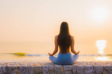 Genç Asyalı kadının portresi sağlık için gün doğumunda deniz kıyısı okyanusunda meditasyon yapıyor.
