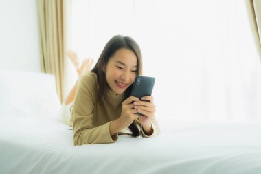 Genç Asyalı kadın yatak odasının iç kısmında cep telefonu kullanıyor.